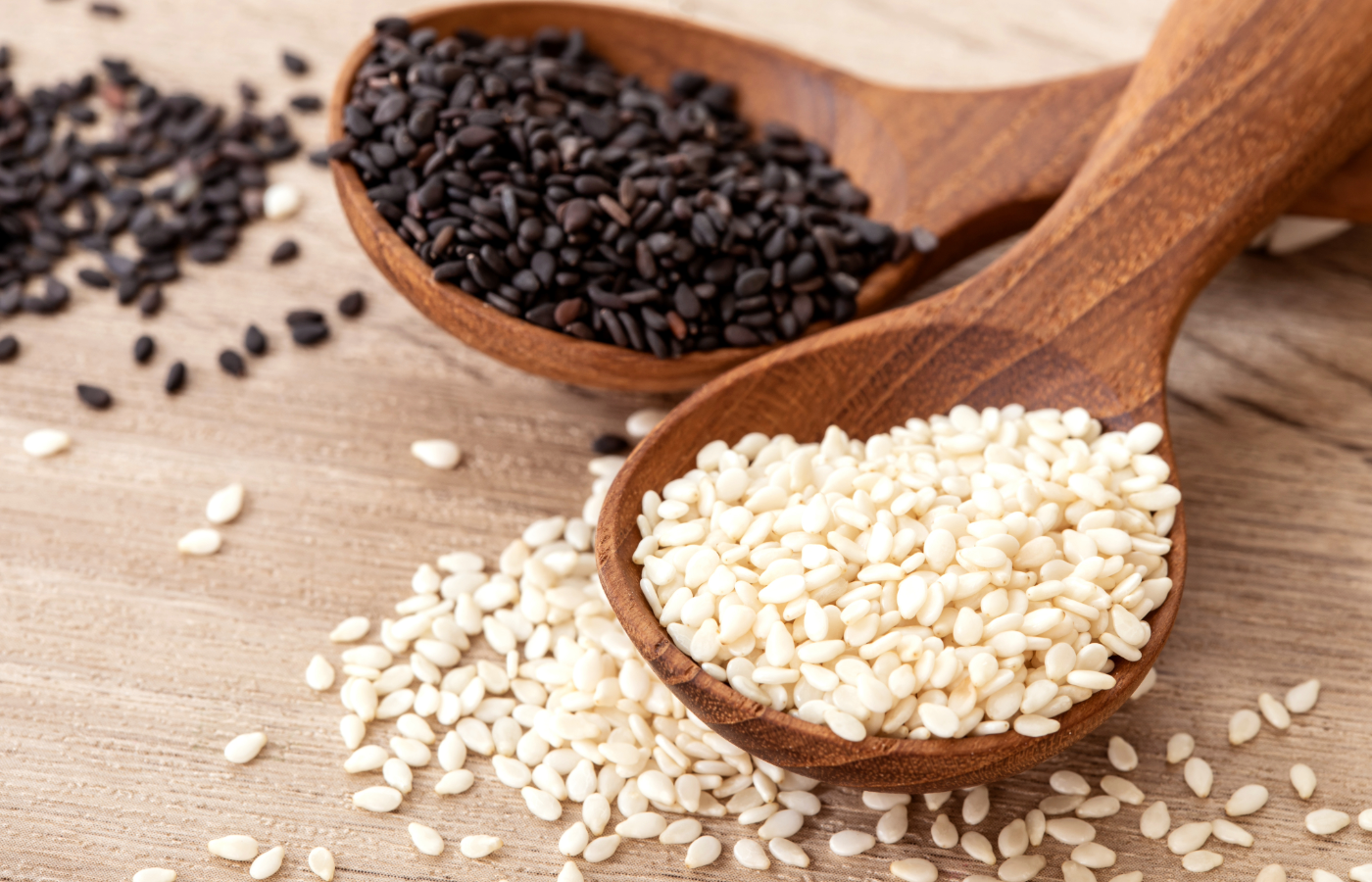 Black sesame seeds white sesame seeds on wooden spoons on a wooden table